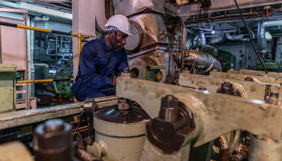 Marine engineer inspecting a ship's turbocharger inside the engine room during routine maintenance.